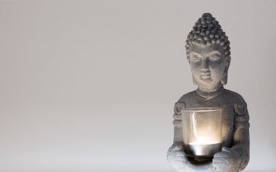 Oberkörper einer Buddha Steinfigur mir Teelicht zwischen den Händen vor weißer Wand